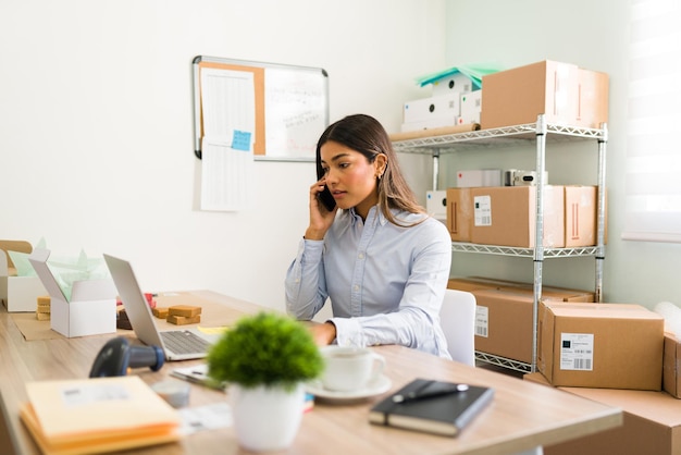 Foto ¿cómo puedo ayudarte con tu pedido? joven latina respondiendo preguntas de un cliente por teléfono en su tienda de productos de belleza natural