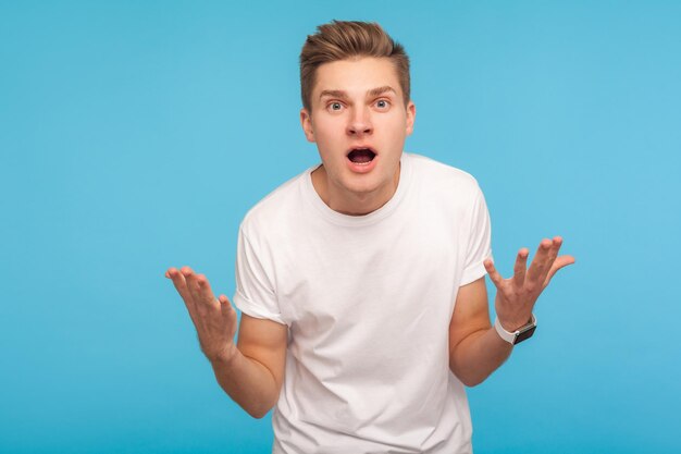 Como você poderia retrato de homem chateado irritado em camiseta brigando com expressão indignada pedindo motivo para erro mal-entendido conceito estúdio interior tiro isolado em fundo azul