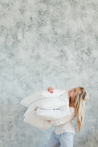 Comodidad de la almohada. Joven mujer rubia satisfecha con montón de almohadas.