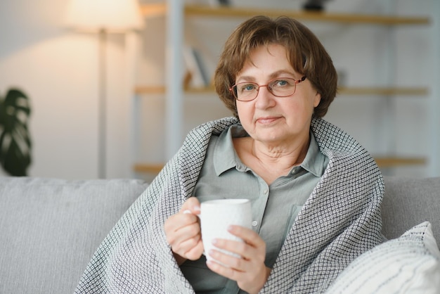 Comodidad relajada anciana anciana abuela bebiendo bebidas calientes té café en casa mirando a la cámara en la sala de estar Concepto de pensión