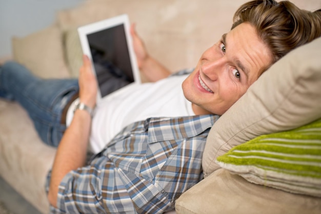 Comodidades de las criaturas Foto de un apuesto joven usando su tableta digital mientras se relaja en el sofá