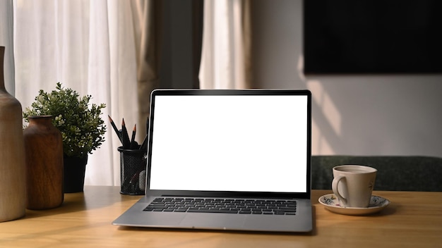 Cómodo lugar de trabajo con computadora portátil, taza de café y planta de interior en un escritorio de madera