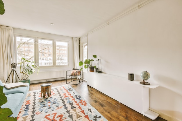 Cómodo sofá ubicado cerca de la alfombra y la mesa contra el estante en una espaciosa sala de estar de estilo luminoso en un apartamento moderno