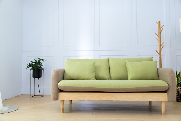 Cómodo sofá verde manzana con almohadas en el espacioso salón interior con espacio de copia en la pared blanca vacía.