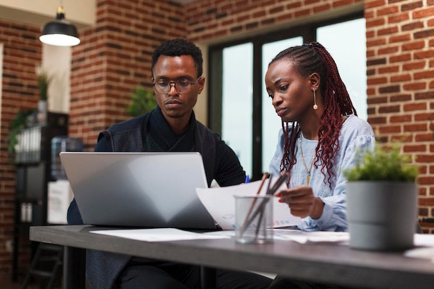 Compañeros afroamericanos de la compañía en una reunión sobre el estado financiero del proyecto de inicio. Gente de negocios en el escritorio del departamento de finanzas de la oficina de la agencia hablando de gastos de marketing.