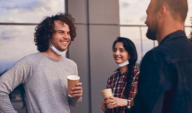 Compañeros alegres en máscaras charlando durante la pausa para el café