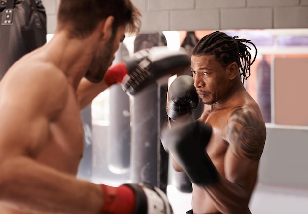 Compañeros de boxeo dedicados Captura de un joven boxeador practicando su puñetazo con un compañero