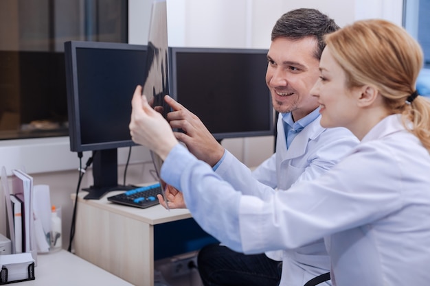 Foto compañeros de buena apariencia positivos alegres mirando la radiografía y sonriendo sin tener nada serio con lo que lidiar