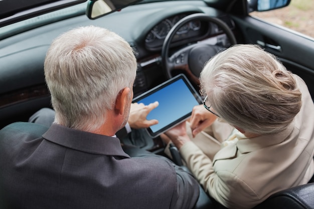 Compañeros maduros trabajando juntos en tableta en coche con clase