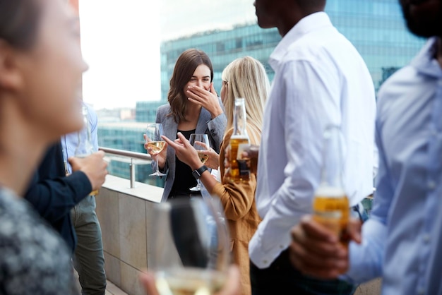 Compañeros de oficina socializando con bebidas en un balcón de la ciudad después del trabajo