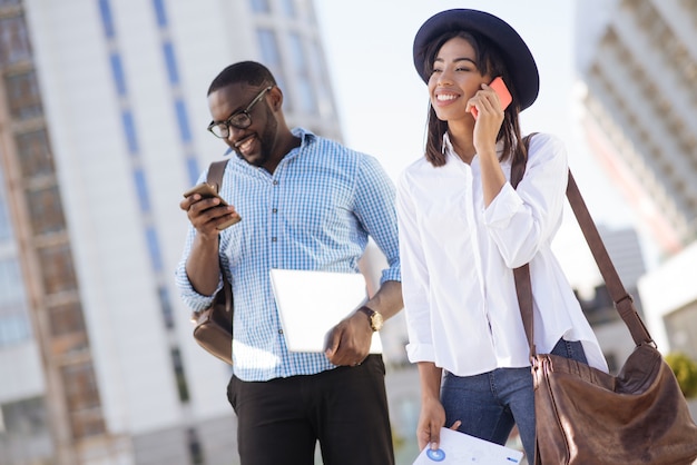 Compañeros productivos y trabajadores persistentes que parecen entusiasmados mientras realizan negociaciones con inversores potenciales usando sus teléfonos