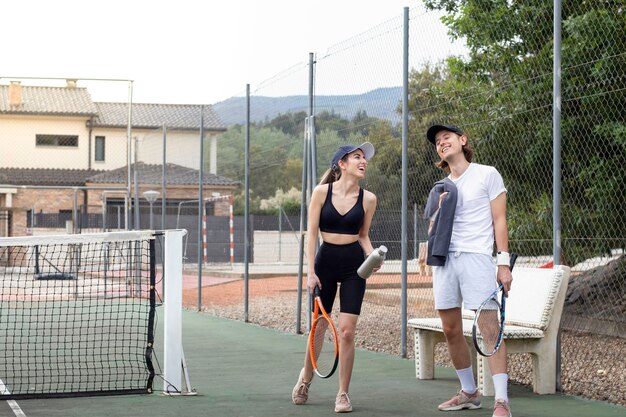 Foto compañeros de tenis caminando por una cancha de tenis con ropa casual riendo apenas mientras se divierten