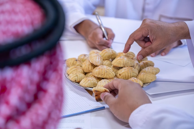 Compañeros de trabajo árabes manos comiendo eid kahk juntos en el escritorio de trabajo