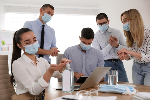 Compañeros de trabajo con máscaras protectoras usando desinfectante para manos en la oficina Reunión de negocios durante la pandemia de COVID19