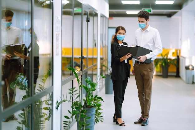 Compañeros de trabajo con mascarilla médica discutiendo juntos cuestiones de trabajo en la oficina. Trabajo en equipo durante la pandemia en la ciudad en cuarentena. COVID-19.