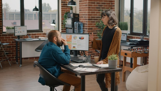 Compañeros de trabajo mirando el monitor con gráficos de tasa de datos para planificar el proyecto y la estrategia de marketing. Colegas que trabajan con computadoras para crear análisis de datos en exhibición para presentaciones comerciales