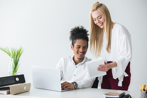 Compañeros de trabajo multiétnicos jóvenes felices que trabajan con dispositivos digitales en la oficina