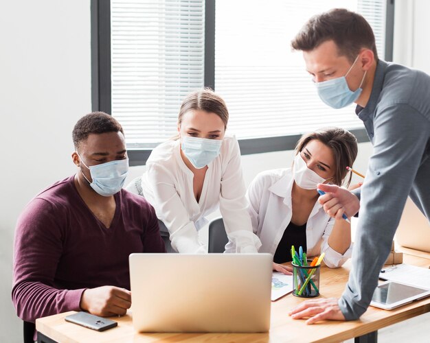 Compañeros de trabajo en la oficina durante la pandemia mirando portátil con máscaras