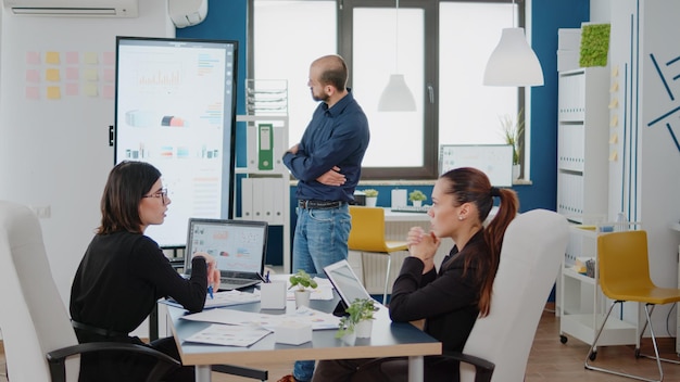 Compañeros de trabajo que se unen a la reunión de negocios para informar y planificar el proyecto. Colegas que usan laptop, tableta y televisión con gráficos de datos para ideas y estrategia de marketing en el espacio de investigación.