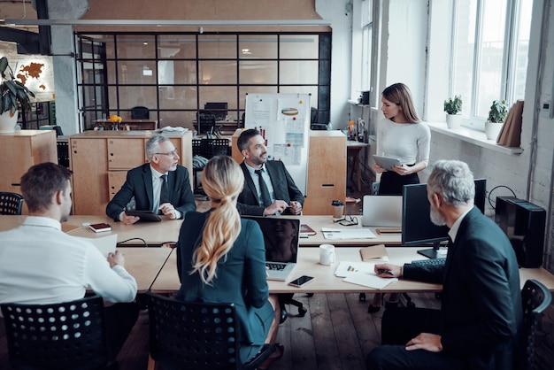 Compañeros de trabajo en ropa formal elegante discutiendo nuevas ideas de negocios mientras trabajan en la oficina moderna