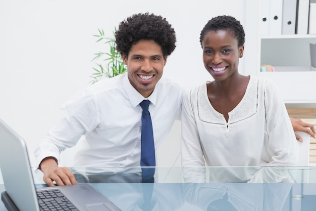 Compañeros de trabajo sonrientes que se sientan y que miran la cámara