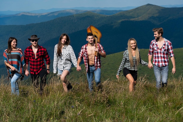 Companhia de jovens amigos ativos de meninos e meninas caminhando no festival de música de verão da montanha