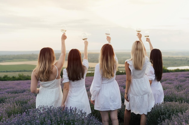 Companhia de mulheres em vestidos brancos seguram taças de vinho em um campo de lavanda