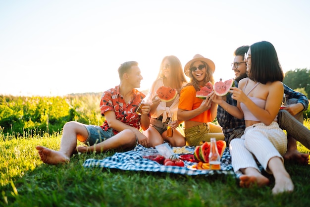 Foto compañía alegre en el prado soleado en el picnic está descansando bebiendo cerveza aclamación concepto de vacaciones