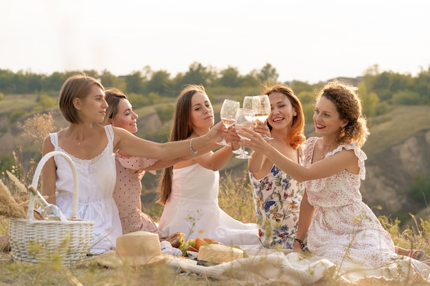 La compañía de amigas disfruta de un picnic de verano y levanta copas con vino.