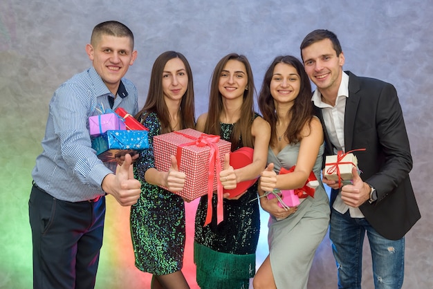 Compañía de amigos celebrando el año nuevo. Mujeres y hombres con coloridas cajas de regalo sobre fondo abstracto