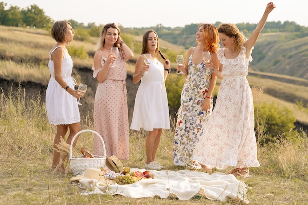 La compañía de hermosas amigas se divierte y disfruta de un picnic de verano, baila y bebe alcohol. Concepto de personas