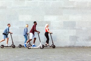 Foto la compañía interracial de amigos monta scooters eléctricos contra el fondo de una pared, la gente usa el transporte ecológico en la ciudad