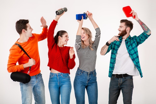 Compañía joven inconformista de amigos divirtiéndose juntos sonriendo escuchando música en altavoces inalámbricos