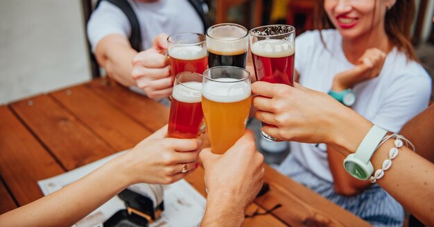 Una compañía de jóvenes amigos multiétnicos tintinean vasos con diferentes cervezas en la terraza de un restaurante