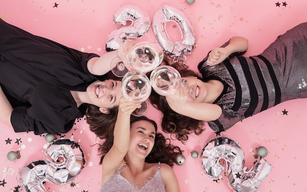 Foto una compañía de novias divirtiéndose en una fiesta de navidad recostada sobre un fondo rosa con copas de champán, año nuevo 2022.