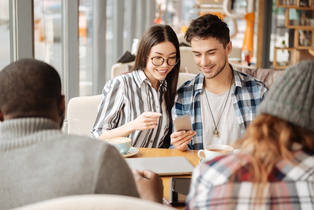 Comparando o número de seguidores. belo casal usando smartphone juntos durante uma reunião com amigos internacionais.