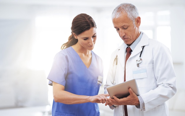 Comparando registros médicos Foto de dois profissionais médicos olhando para um tablet digital