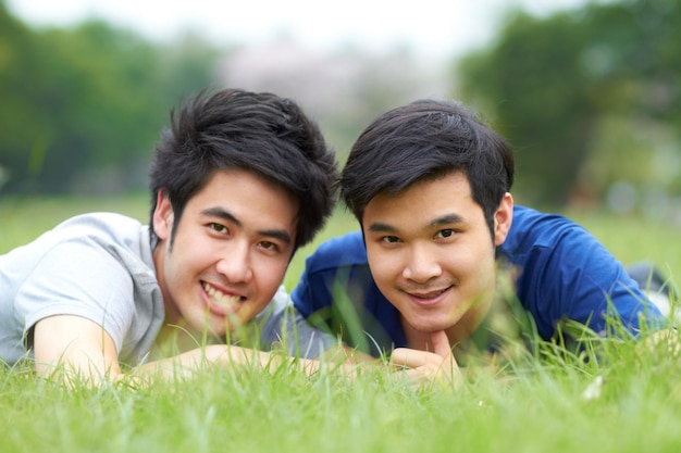 Comparten el amor por el aire libre Una linda pareja asiática gay joven sonriendo juntos mientras están tumbados en el césped