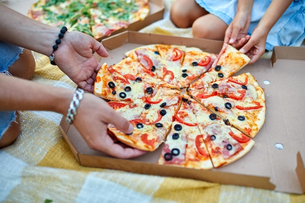 Compartilhando as mãos de pizza pegando um pedaço de pizza de uma caixa de piquenique em família ao ar livre comendo pizzas para o jantar entrega de fast food