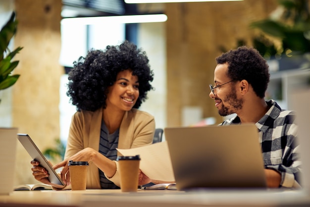 Foto compartilhando novas ideias, dois jovens empresários multirraciais felizes sentados na mesa e se comunicando