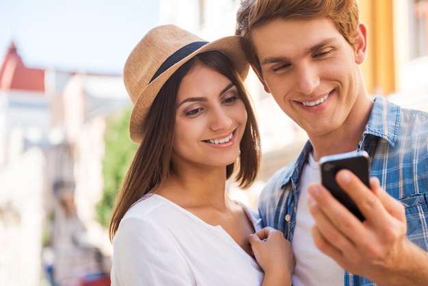 Compartilhando suas fotos com amigos. jovem casal apaixonado em pé perto um do outro enquanto um homem segurando um telefone celular e sorrindo