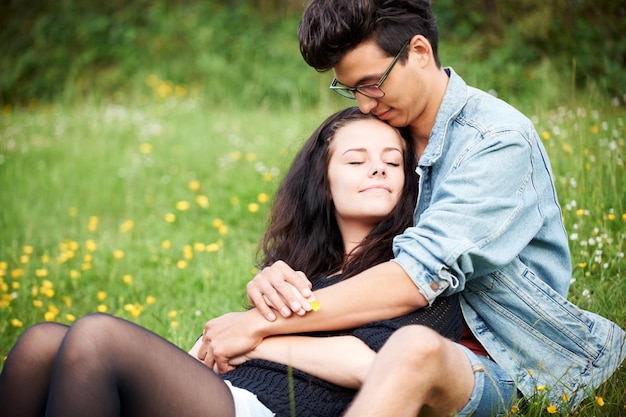 Compartilhando um vínculo doce Jovem casal sentado afetuosamente em um campo de primavera