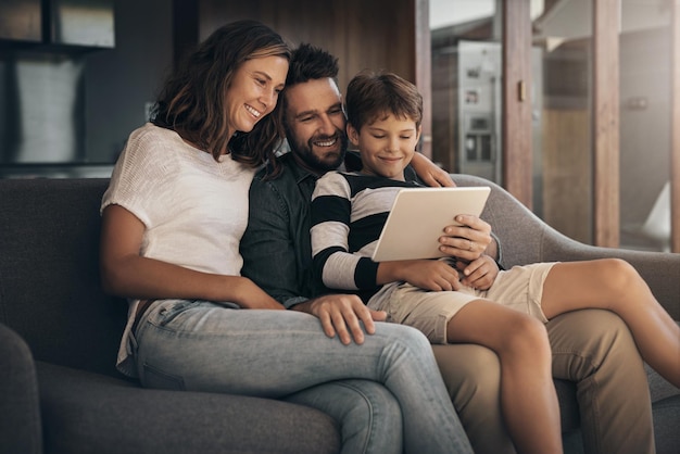 Compartilhe o amor compartilhe a diversão Foto de um garotinho adorável usando um tablet digital com sua mãe e seu pai no sofá em casa