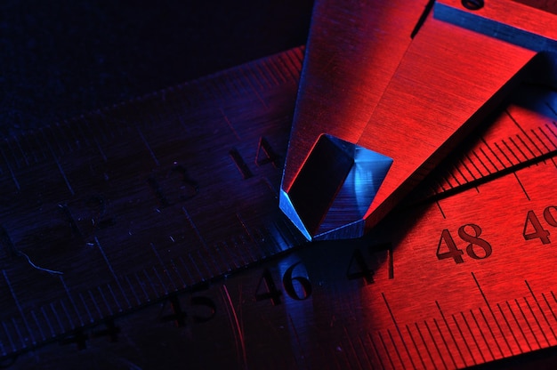 Compasso de calibre e réguas de metal iluminadas em closeup vermelho e azul