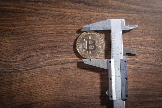 Compasso de calibre vernier e Bitcoin na mesa de madeira