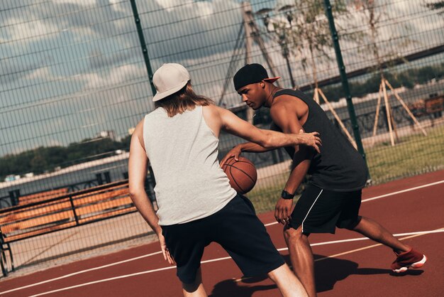 Competencia. Dos hombres jóvenes en ropa deportiva jugando baloncesto mientras pasan tiempo al aire libre