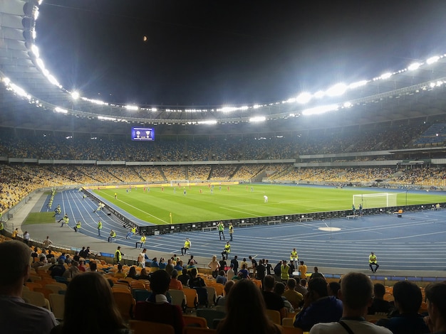 Competição de futebol em um grande estádio à noite com um destaque brilhante removido das arquibancadas