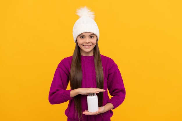 Complemento alimenticio jovencita con productos de píldoras naturales que presenta tabletas multivitamínicas de productos vitamínicos para niños estilo de vida saludable salud infantil niño feliz con sombrero de invierno con tarro de píldoras