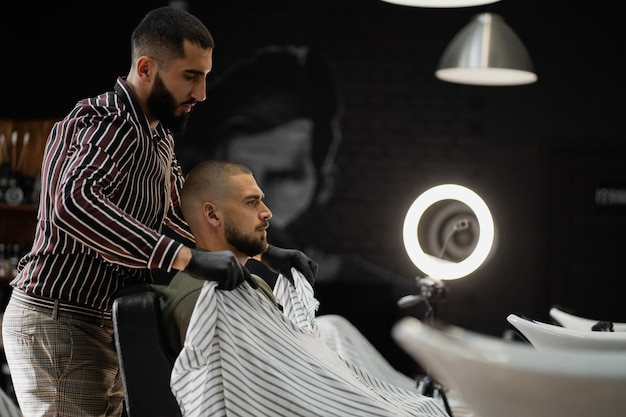 Completando el corte de pelo de un joven de aspecto brutal con barba profesional