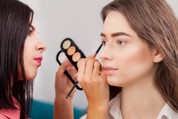 Compõem o artista fazendo maquiagem profissional de jovem perto do espelho no estúdio de beleza